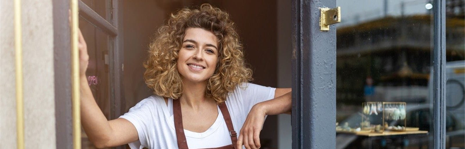 Eine Frau trägt eine braune Schürze und schaut aus ihrem Ladengeschäft.